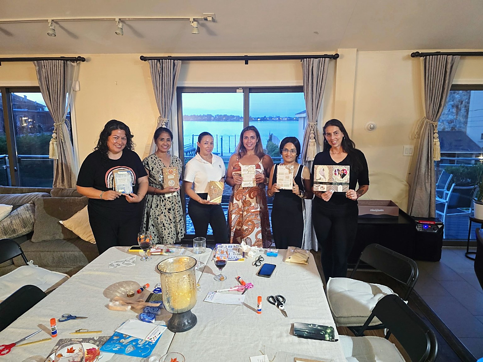 Six women holding their finished journals at a My Craft Studio gathering by the water